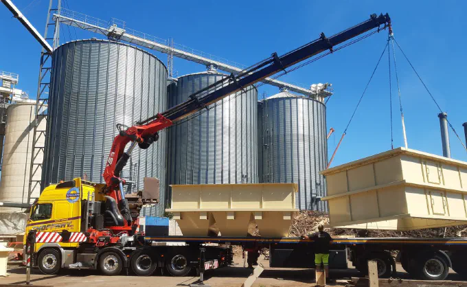 Tracteur grue HIAB levant des trémies près des silos